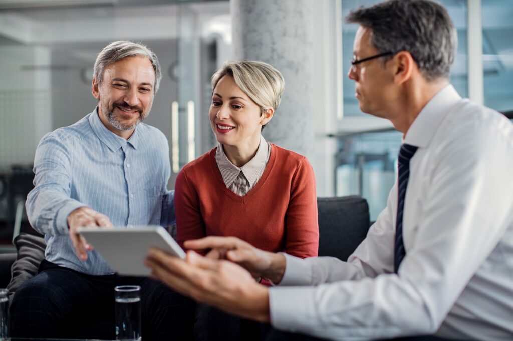 happy mid adult couple using touchpad with their financial consultant in the office